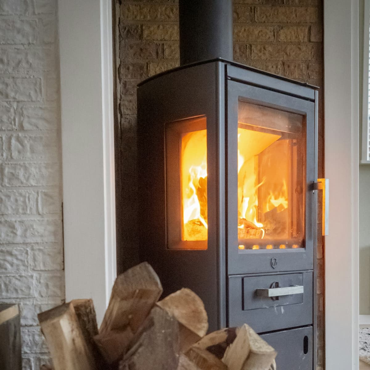 A wood stove with a fire burning and a basket of split firewood beside it